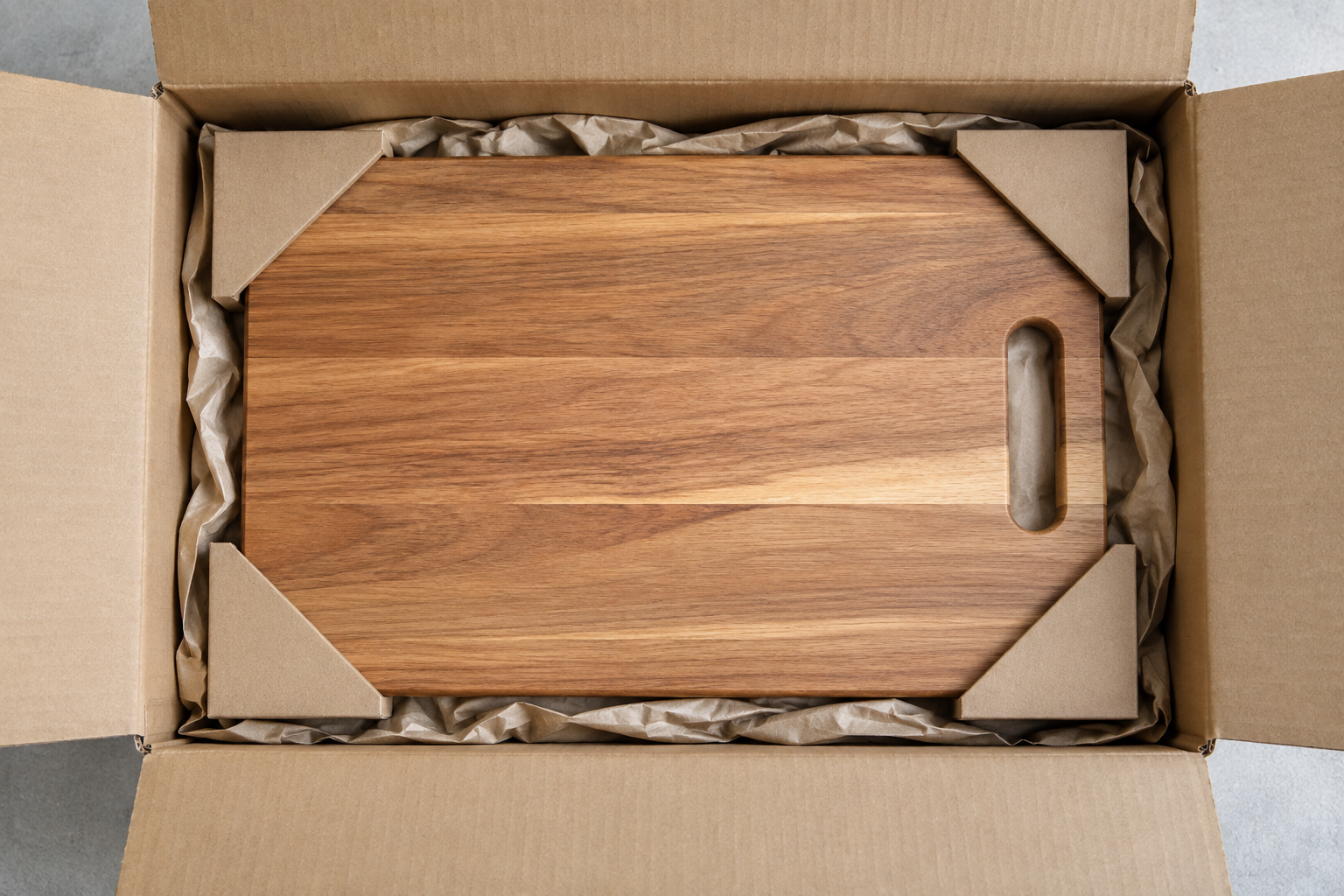 Wooden cutting board in a plain open cardboard carton with kraft paper and corner protectors