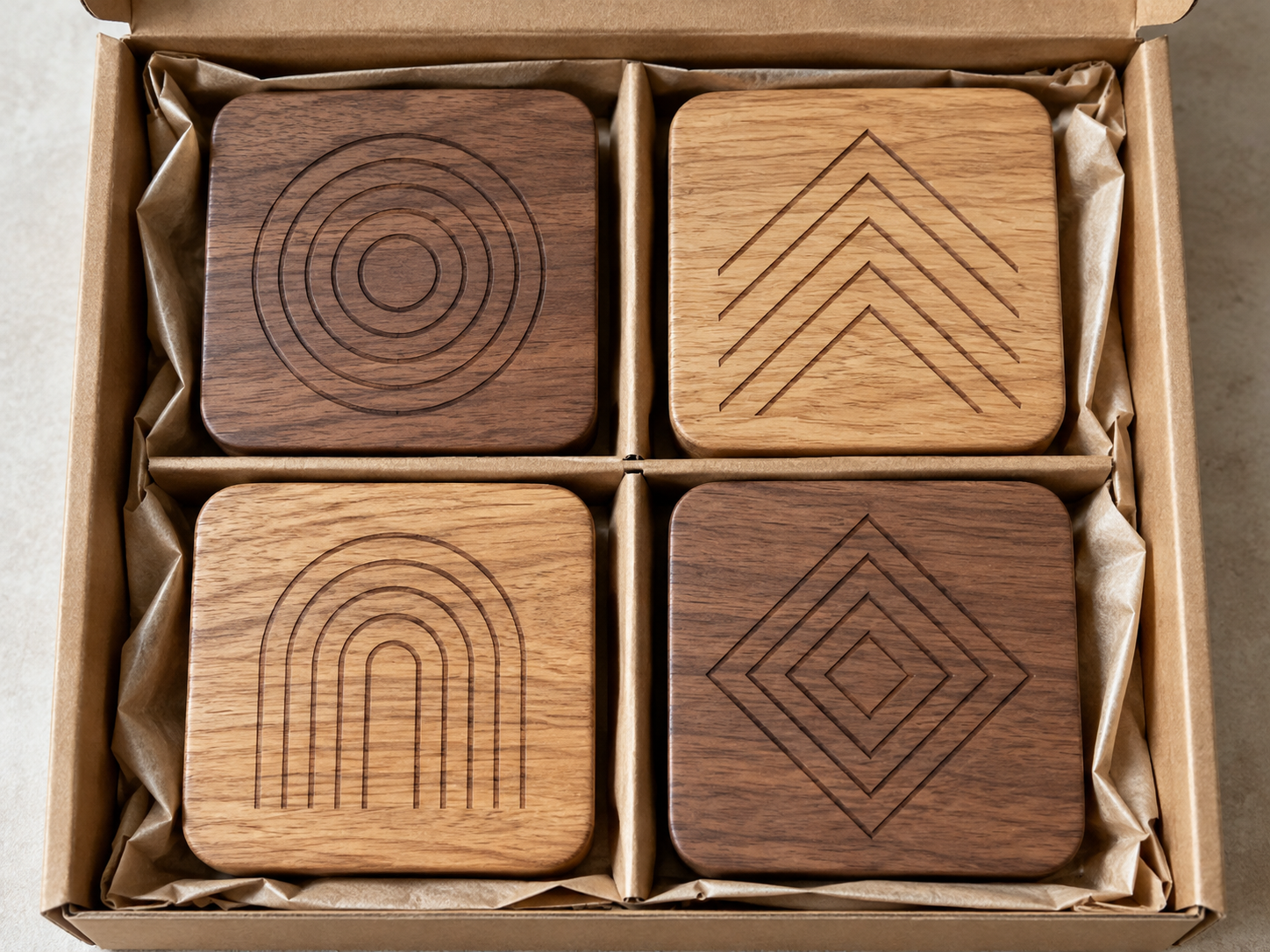 Four laser engraved wooden coasters with geometric patterns in a plain open kraft cardboard gift box